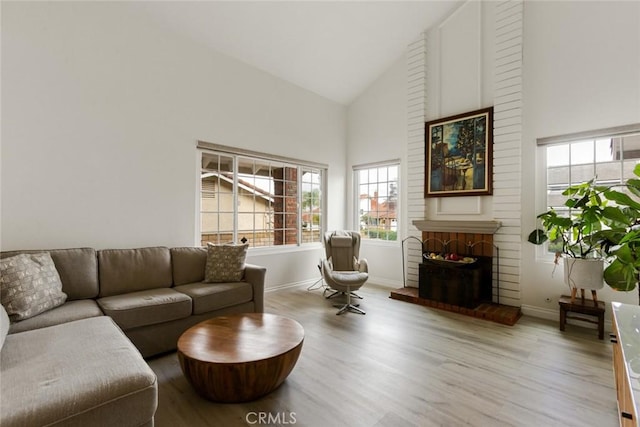 living room with a brick fireplace, high vaulted ceiling, baseboards, and wood finished floors