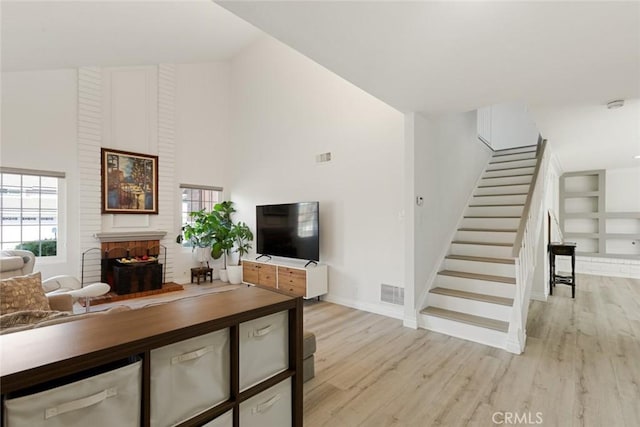 living room featuring visible vents, stairway, light wood-style flooring, a fireplace, and high vaulted ceiling