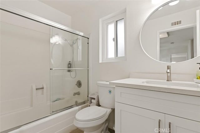 bathroom featuring visible vents, vanity, toilet, and bath / shower combo with glass door