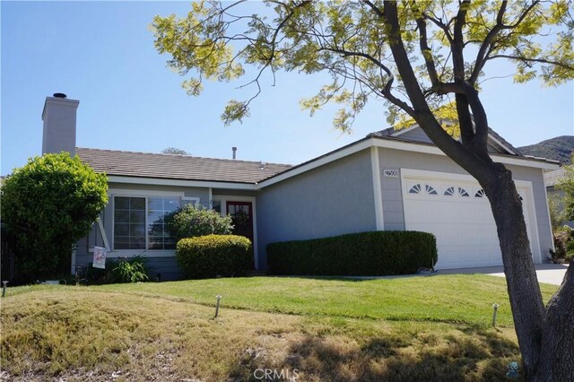 ranch-style home with an attached garage, a chimney, driveway, and a front yard