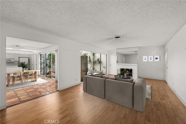 living area with visible vents, a warm lit fireplace, a textured ceiling, and light wood-type flooring