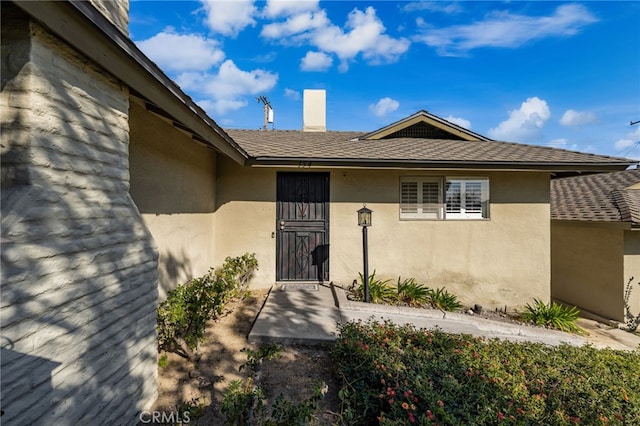 doorway to property with stucco siding and roof with shingles