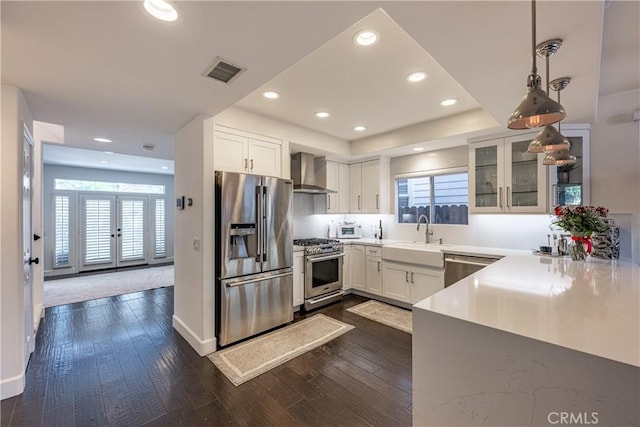 kitchen featuring visible vents, a sink, dark wood-style floors, appliances with stainless steel finishes, and wall chimney exhaust hood