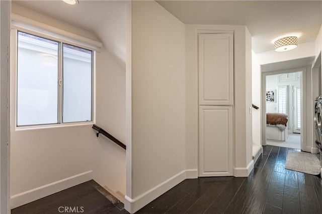 hall with an upstairs landing, baseboards, and dark wood-style flooring