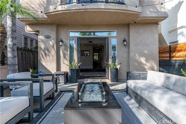 property entrance featuring a balcony, fence, stucco siding, outdoor lounge area, and a patio area