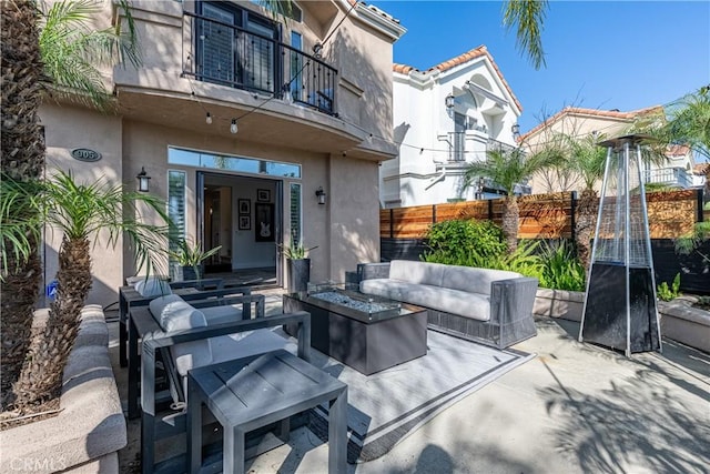 view of patio featuring a balcony, an outdoor living space with a fire pit, and fence