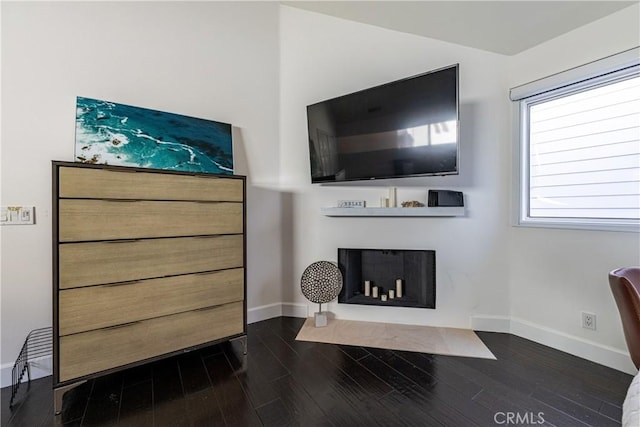 living area featuring a fireplace with flush hearth, baseboards, and dark wood-style flooring