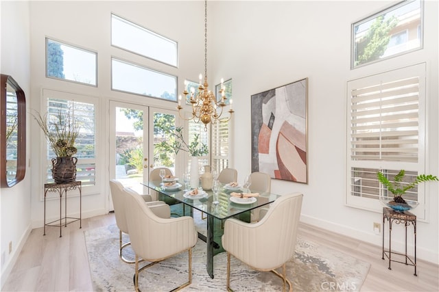 dining space featuring baseboards, a high ceiling, a chandelier, and light wood finished floors