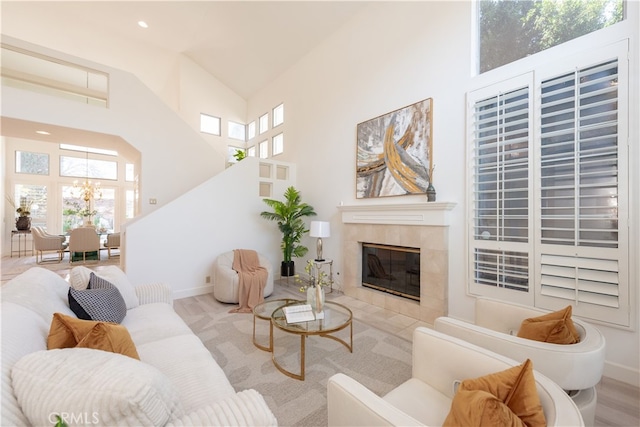 living area featuring baseboards, a tile fireplace, a towering ceiling, and a chandelier