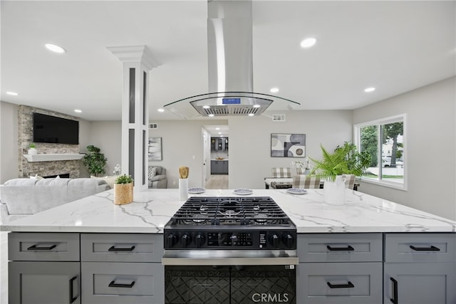 kitchen featuring gray cabinets, open floor plan, gas stove, island range hood, and light stone countertops