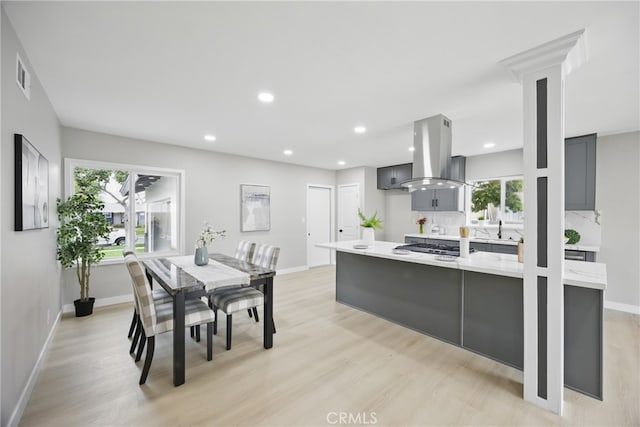 kitchen with light wood finished floors, visible vents, light countertops, island exhaust hood, and a sink