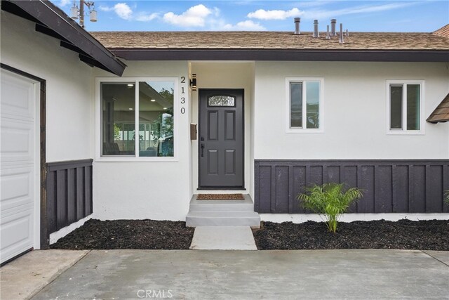 property entrance featuring a shingled roof, an attached garage, and stucco siding