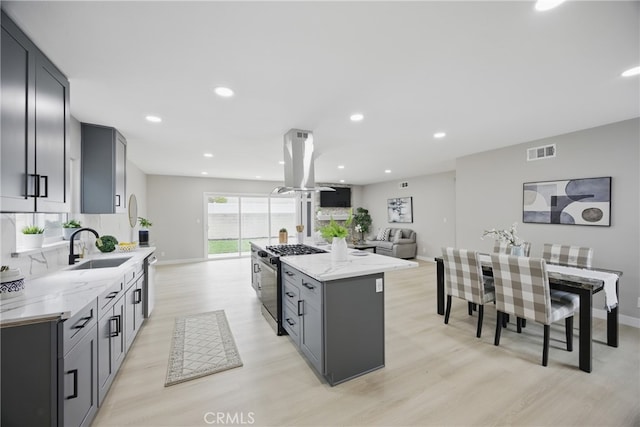 kitchen featuring visible vents, a sink, a center island, gas range oven, and island range hood