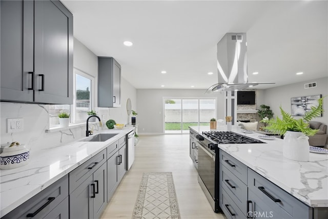 kitchen featuring open floor plan, gray cabinets, island range hood, gas stove, and a sink