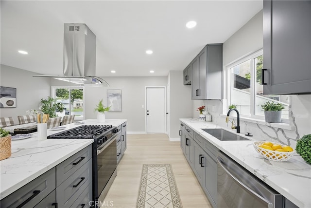 kitchen with light stone countertops, gray cabinets, stainless steel appliances, a sink, and island range hood