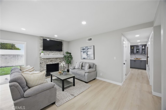 living area with baseboards, visible vents, light wood-style flooring, recessed lighting, and a stone fireplace