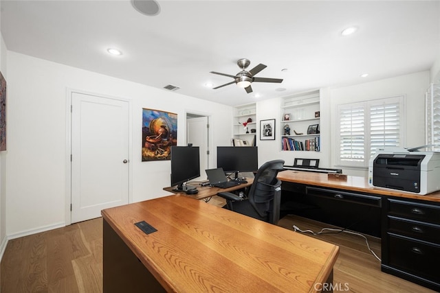 office featuring visible vents, built in shelves, light wood-style flooring, a ceiling fan, and recessed lighting