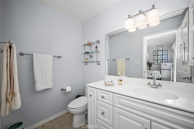 bathroom with vanity, toilet, wood finished floors, and baseboards