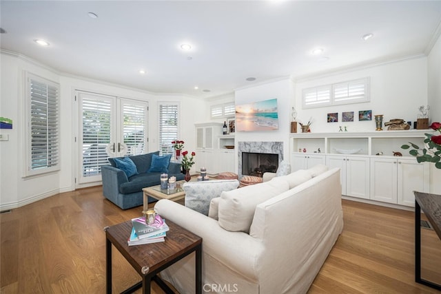 living area with a premium fireplace, light wood-style flooring, recessed lighting, and ornamental molding