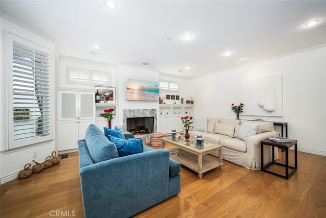 living area featuring wood finished floors, a high end fireplace, recessed lighting, crown molding, and baseboards