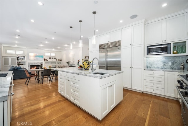 kitchen with built in appliances, a warm lit fireplace, light wood-style flooring, and white cabinetry