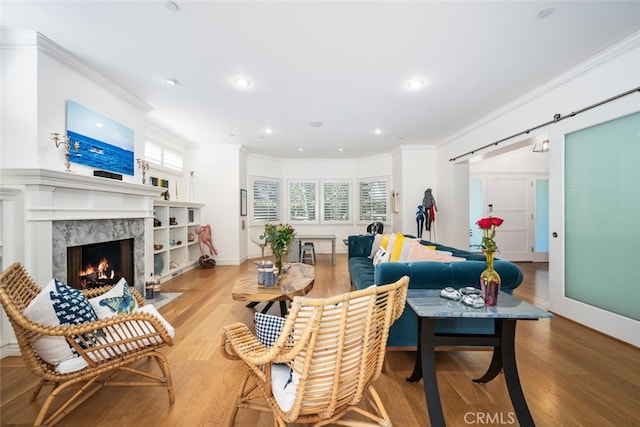 living room with a premium fireplace, a barn door, wood finished floors, and ornamental molding