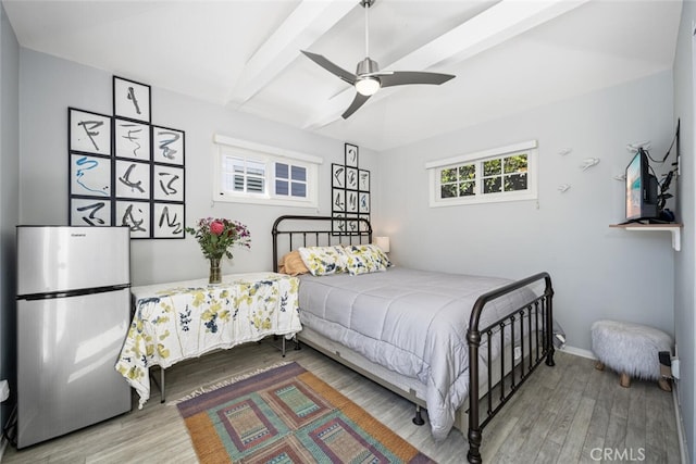 bedroom with a ceiling fan, wood finished floors, baseboards, beam ceiling, and freestanding refrigerator