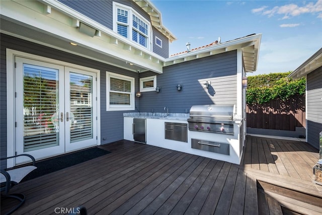 wooden terrace with area for grilling, a sink, fence, french doors, and an outdoor kitchen