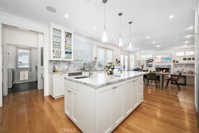 kitchen with a sink, open floor plan, white cabinetry, a lit fireplace, and light wood finished floors