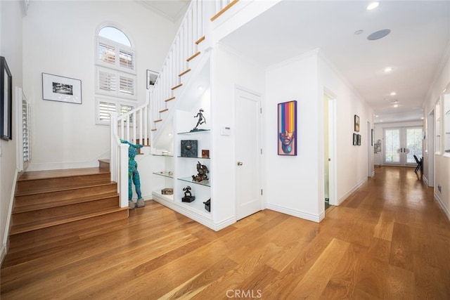 hall with stairs, french doors, light wood-type flooring, and ornamental molding