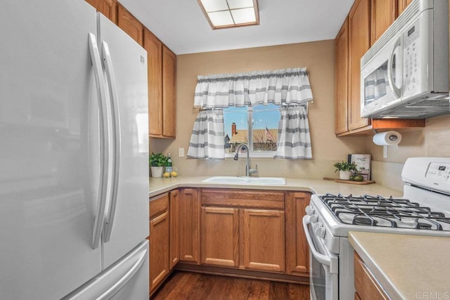 kitchen featuring brown cabinetry, white appliances, light countertops, and a sink