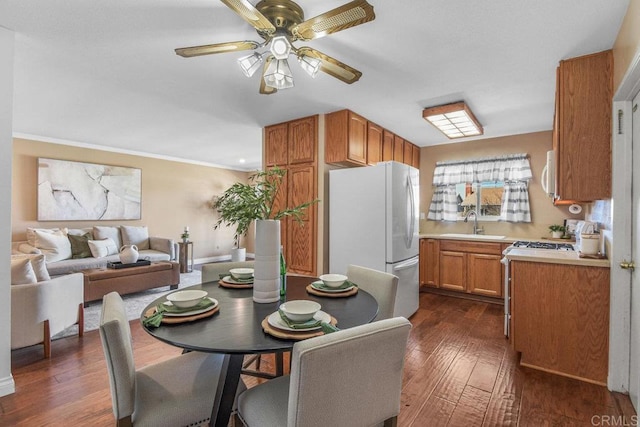 dining area featuring dark wood-type flooring, crown molding, baseboards, and ceiling fan