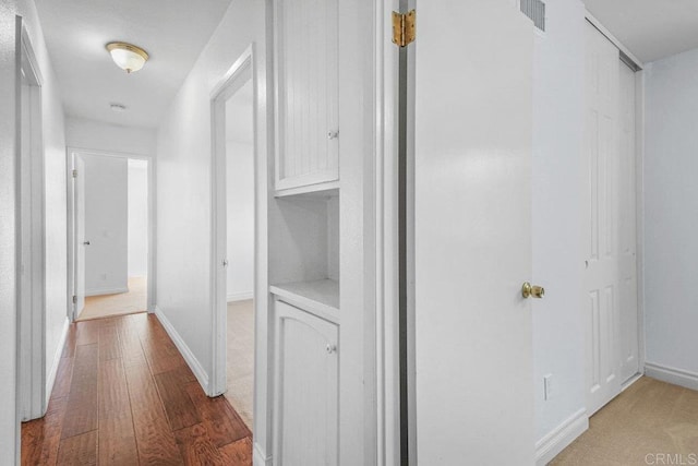 hallway with hardwood / wood-style floors, visible vents, and baseboards