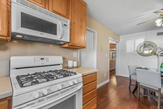 kitchen featuring light countertops, brown cabinets, white appliances, a ceiling fan, and dark wood-style flooring