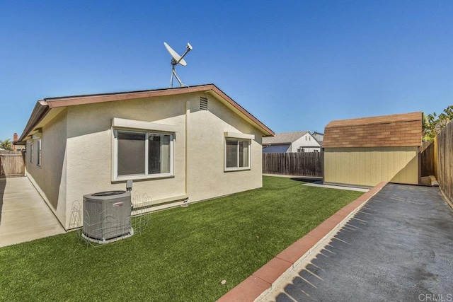 back of house with a fenced backyard, central AC, stucco siding, an outdoor structure, and a storage unit