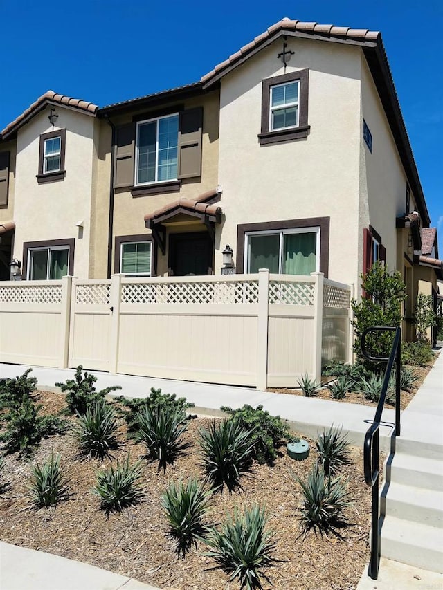 view of front facade with stucco siding, a tile roof, and fence