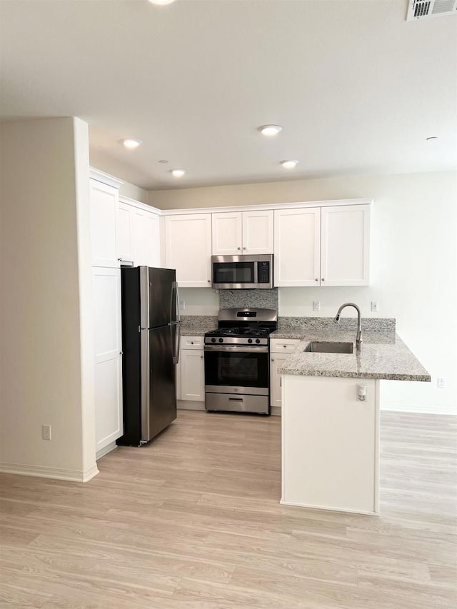 kitchen featuring a sink, appliances with stainless steel finishes, a peninsula, white cabinets, and light stone countertops