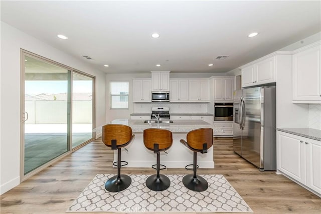 kitchen with visible vents, a center island with sink, light wood-style flooring, appliances with stainless steel finishes, and white cabinets