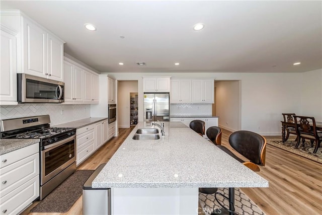 kitchen with light wood-style flooring, a kitchen breakfast bar, white cabinets, stainless steel appliances, and a sink