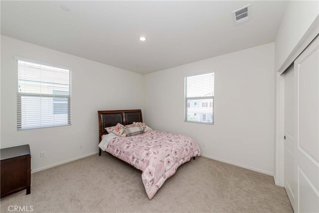 bedroom featuring light colored carpet, visible vents, a closet, and baseboards