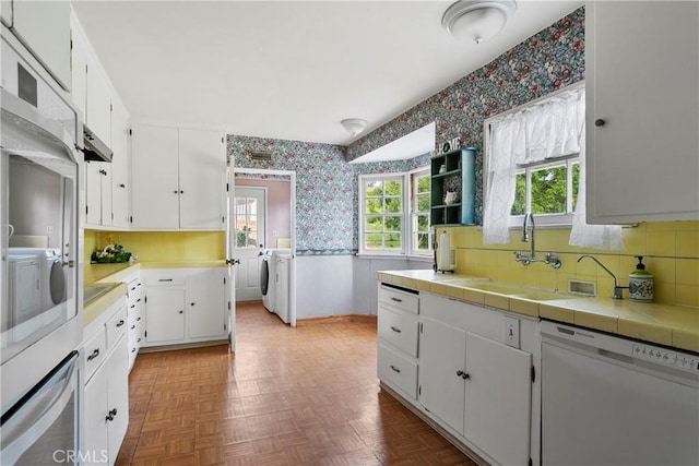 kitchen featuring oven, white cabinets, wallpapered walls, dishwasher, and washing machine and clothes dryer