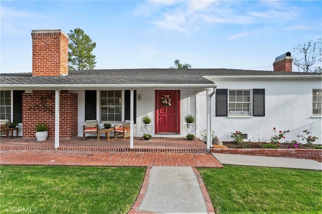 ranch-style home featuring a porch, a front yard, roof with shingles, stucco siding, and a chimney