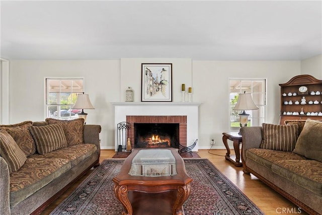 living area with baseboards, light wood-style floors, and a brick fireplace