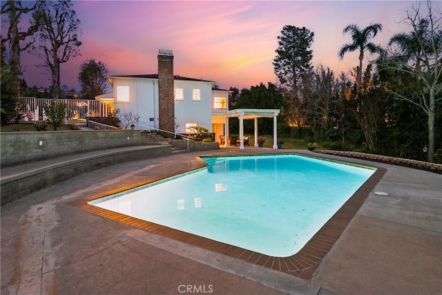 pool at dusk featuring a patio and an outdoor pool