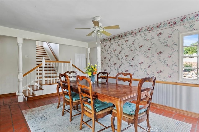 tiled dining room featuring a wainscoted wall, a ceiling fan, stairway, wallpapered walls, and ornate columns