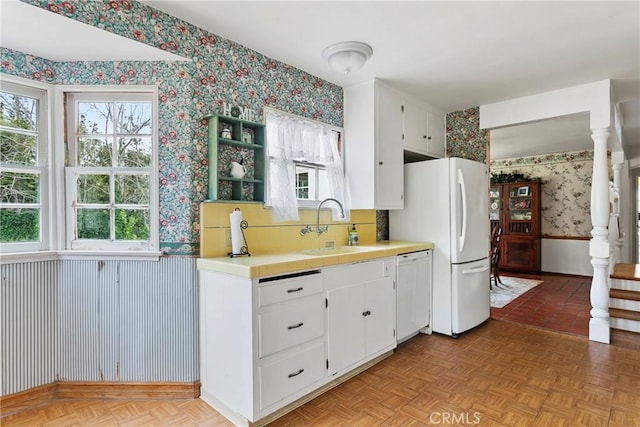 kitchen featuring wallpapered walls, wainscoting, white cabinets, white appliances, and a sink