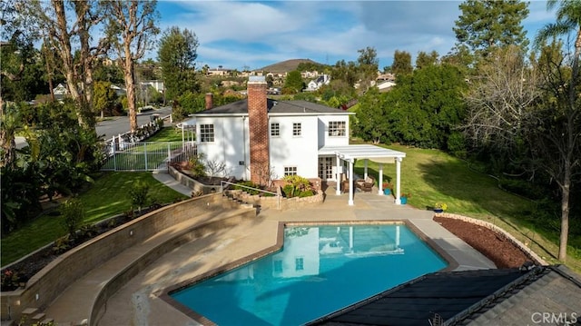 back of property featuring a lawn, fence, an outdoor pool, a chimney, and a patio area