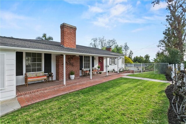 back of property featuring fence, a yard, a shingled roof, brick siding, and a chimney