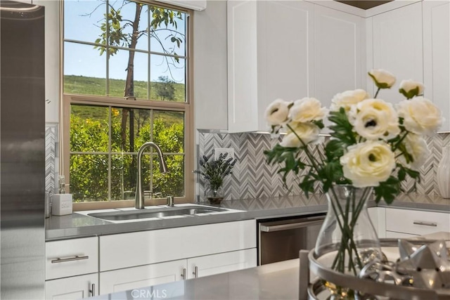 kitchen with a sink, stainless steel counters, tasteful backsplash, stainless steel fridge, and white cabinets