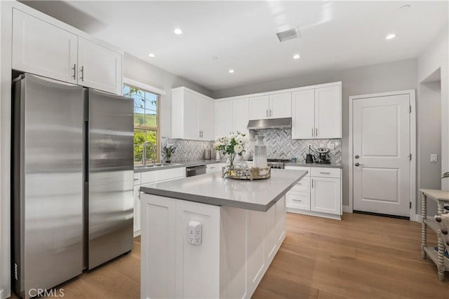 kitchen featuring visible vents, light wood-style flooring, under cabinet range hood, a sink, and appliances with stainless steel finishes